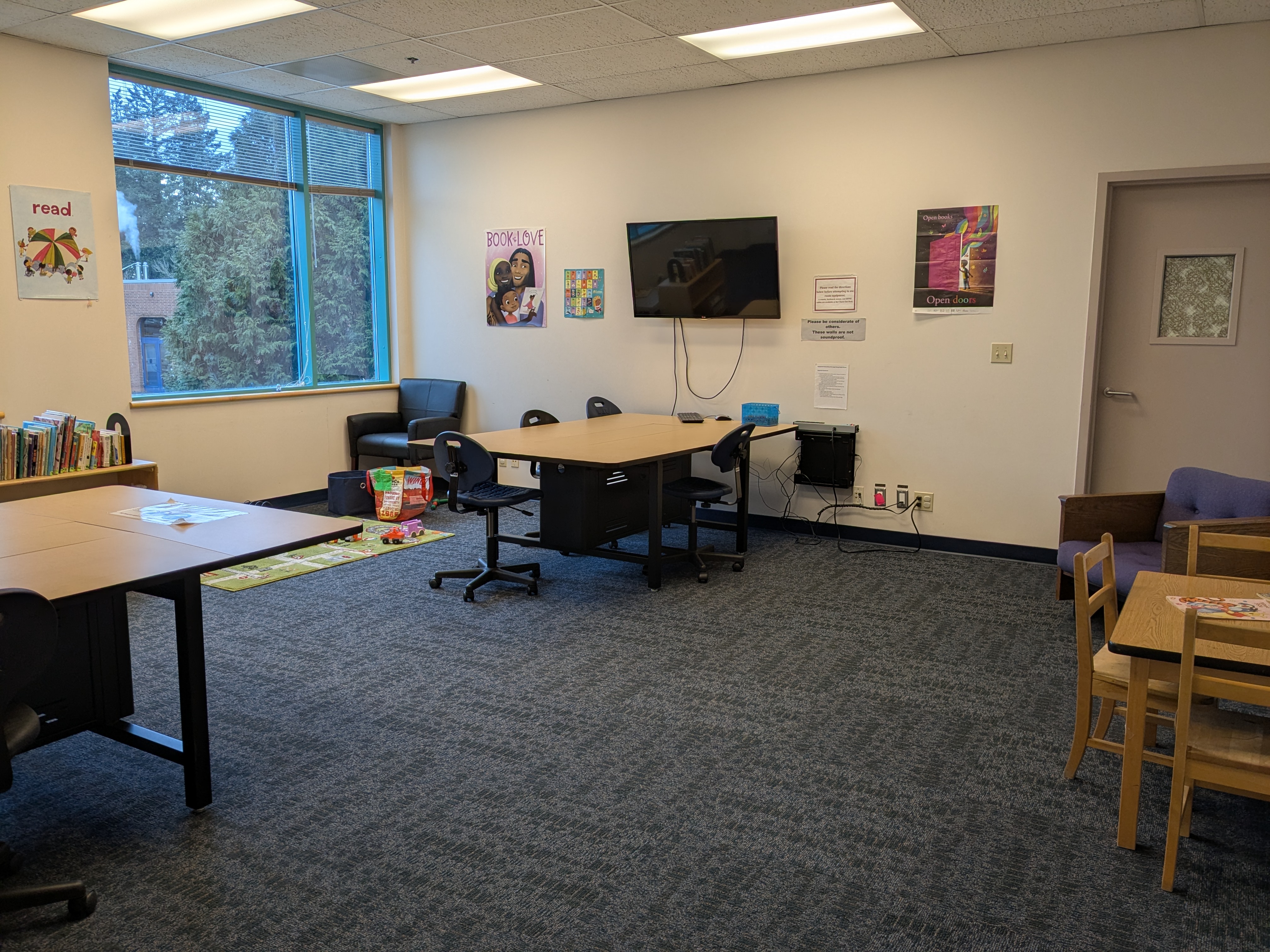 Full room of the family study room with tables for students and kids, a playmat, and bookshelf